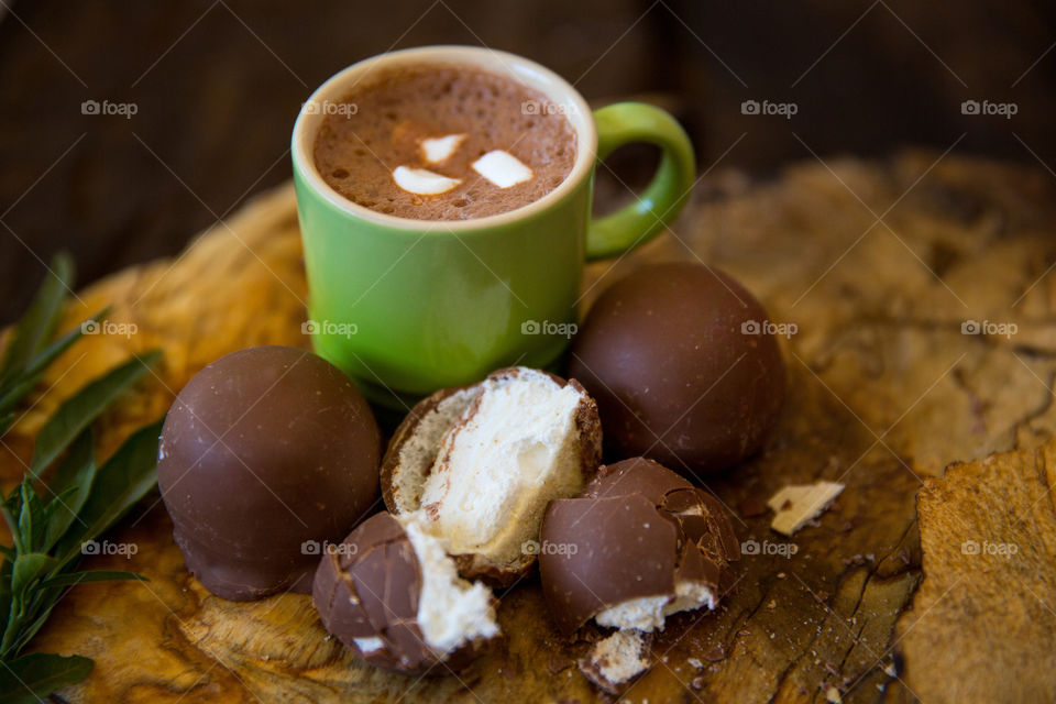 Delicious sweet hot chocolate with marshmallow and marshmallow filled milk chocolates on a wooden background.