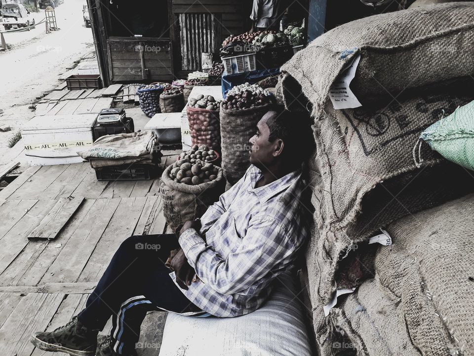 A worker leaning and relaxing over sacks of goods he just unloaded