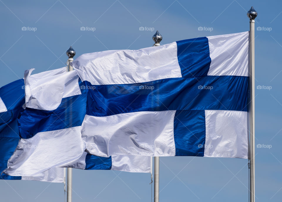 Three Finnish flags flying on sunny spring evening with blue sky in the background.