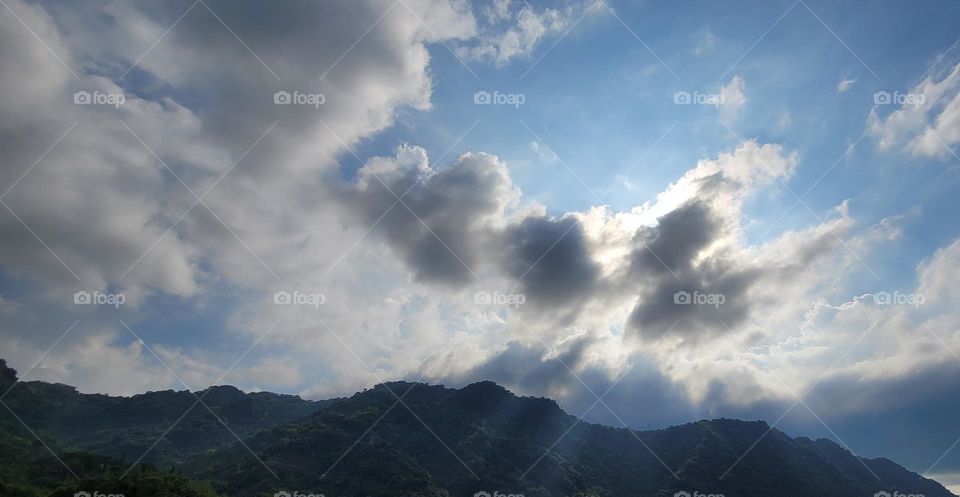 The sun shines through the clouds on the mountains