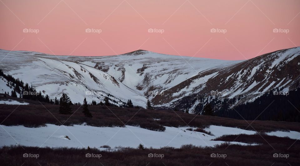 A bright pink sky sets the scene for this high alpine mountain covered in snow during the cold winter.
