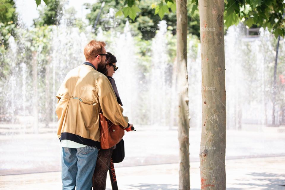 Couple sharing a scooter ride with a fountain in the background