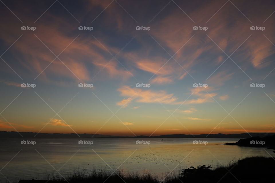 Orange horizon and pink clouds after sun setting behind the calm ocean on a perfect autumn day