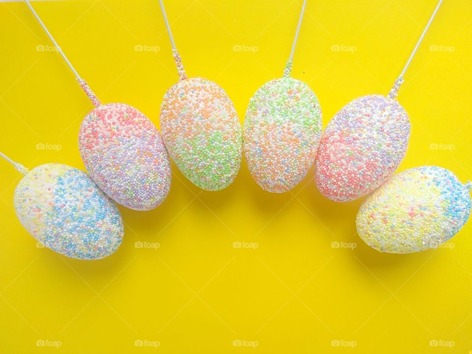 six colorful easter eggs on sticks on a yellow background