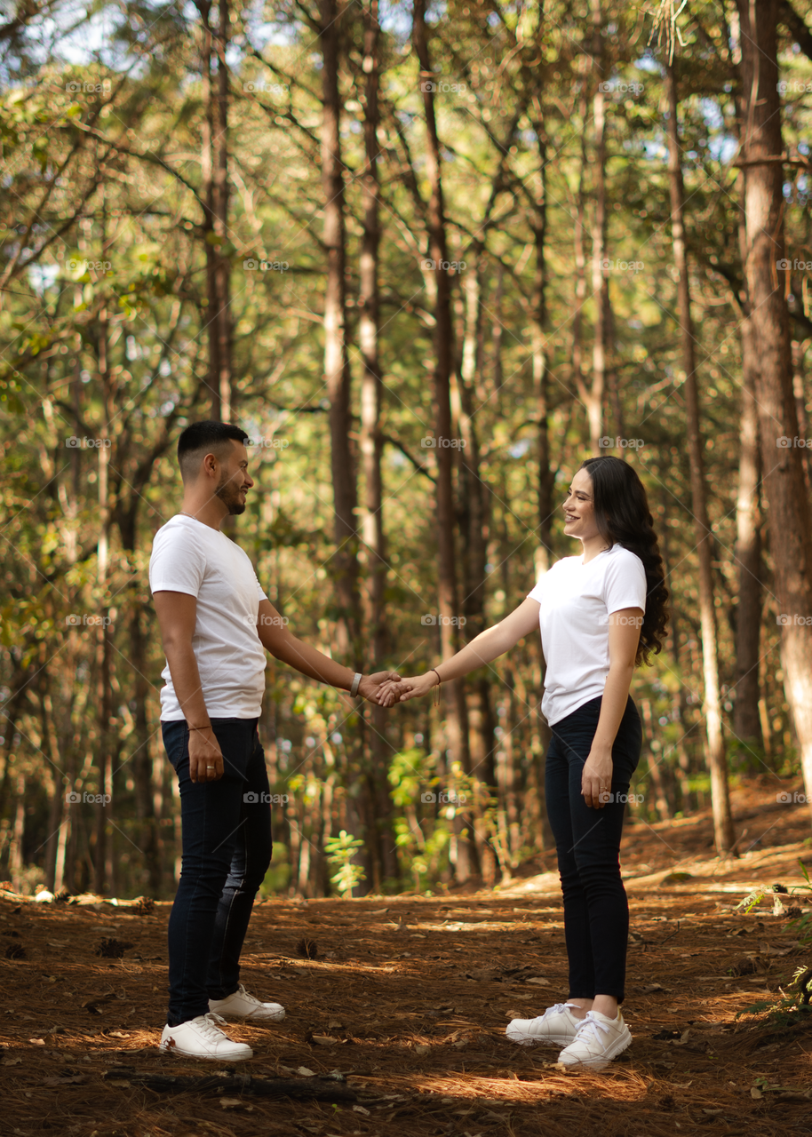 Couples of young people sitting in middle of the forest while looking into their eyes, in a sunny day.