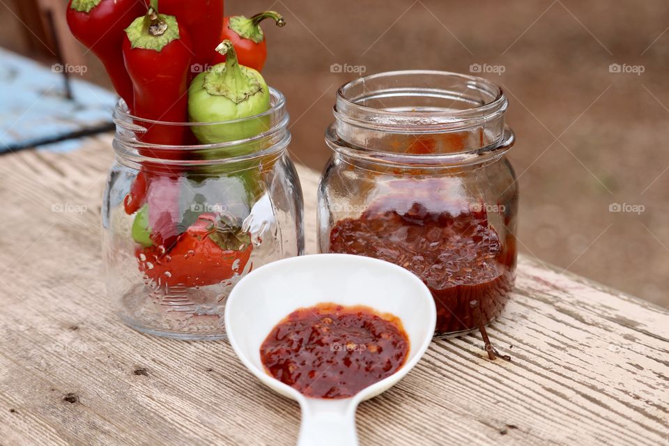 Homemade food red pepper preserves, outdoor rustic, pint jar, fresh peppers and white ladle full of the preserves 