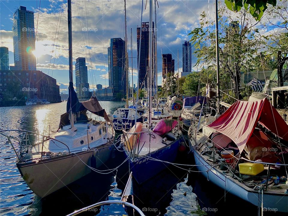This is “Newtown Creek” by the “Pulaski Bridge” in LIC, Queens with all the boats that are tied to the shore here. It is the golden hour of sunset right before  twilight time and the sunlight is reflected back by the ocean. 2023. Hypnotic Productions