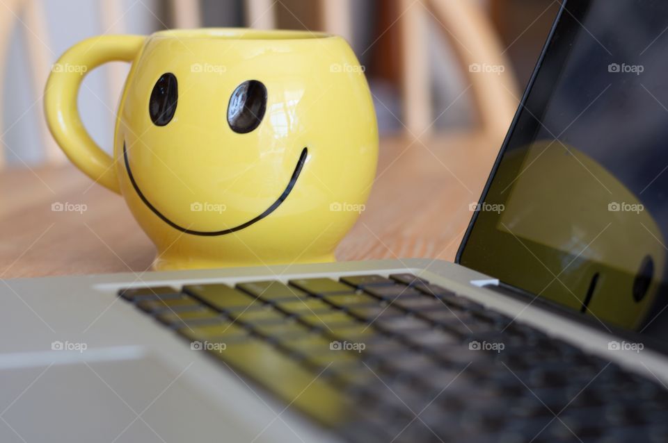 Morning coffee and computer. Smiley face coffee cup next to a laptop computer.