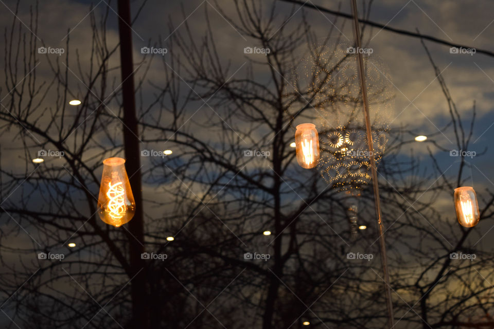 A foto foi tirada de uma parede de vidro espelhada de um restaurante. Assim, só aparece três lâmpadas e um lustre que pertencem ao local, em meio a uma árvore seca e o céu refletidos.