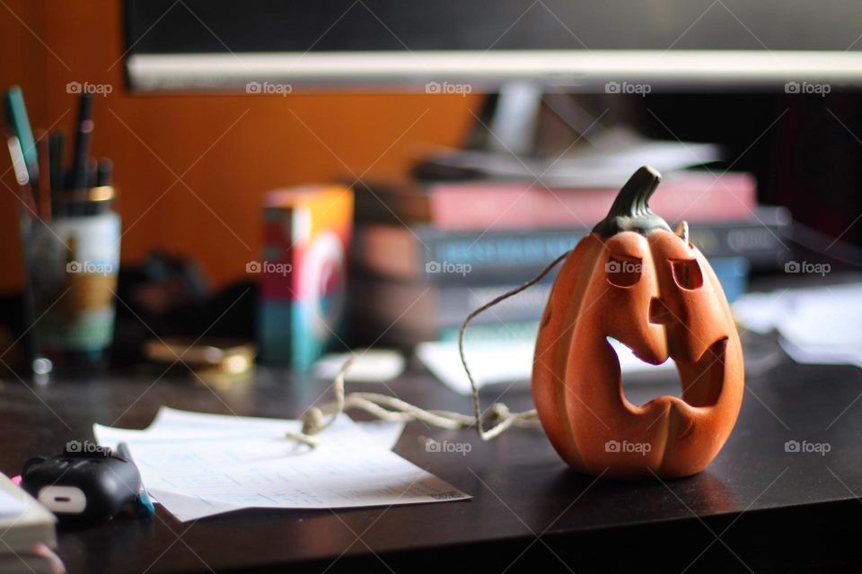 A small orange Halloween pumpkin stands on a black desk with office supplies and a screen
