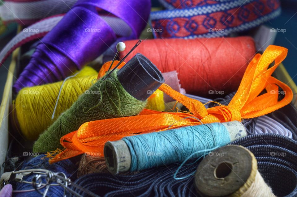 sloppily messed up multicolored spools of thread ribbons and needles dot needlework sewing theme.