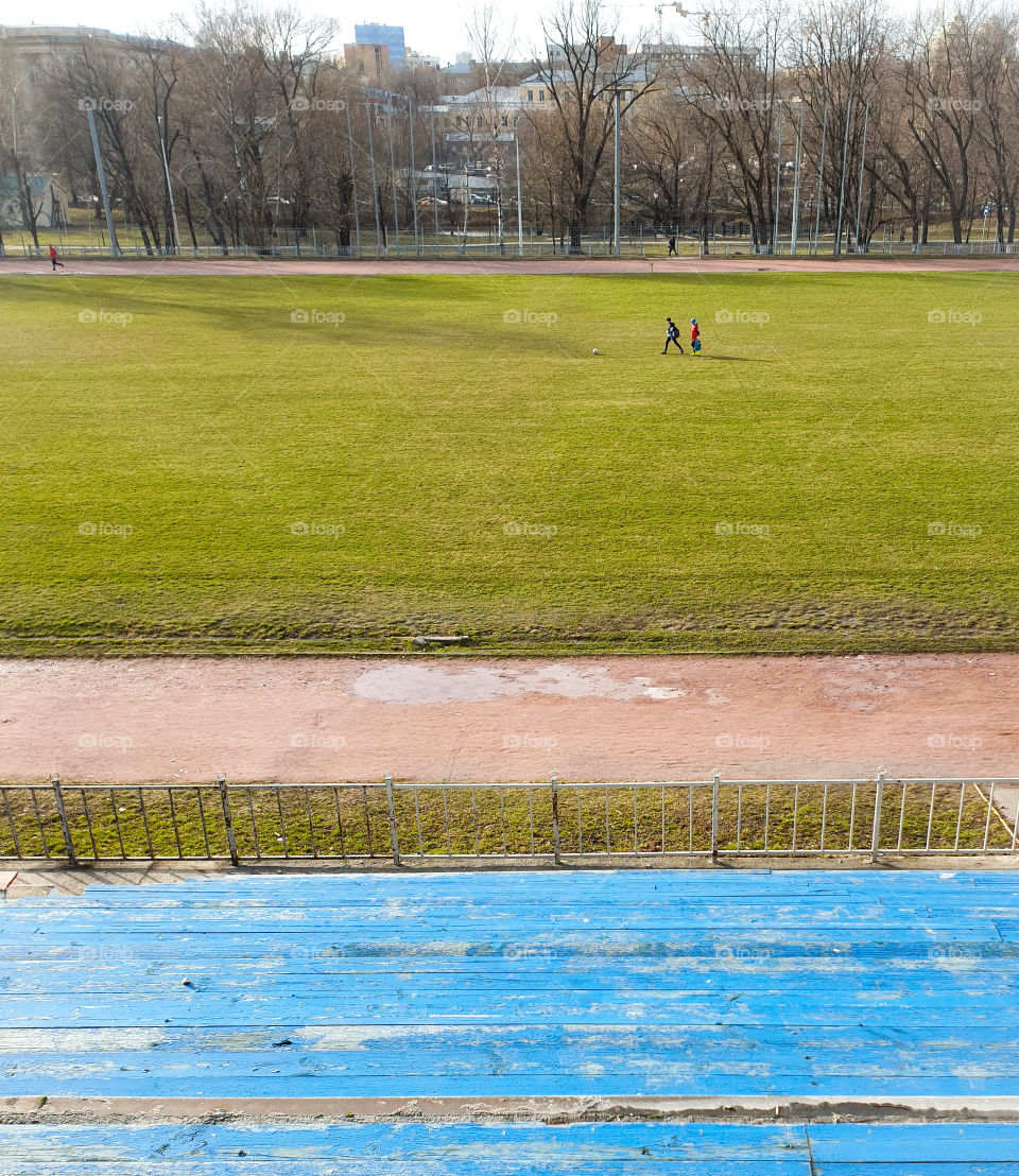 The beginning of spring, a boy with a girl on the football field playing ball.  View from the podium on an open football field with young grass and children playing ball
