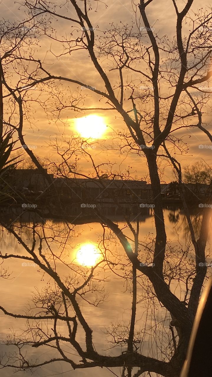 Heading Into Evening High Clouds Partly Separated parting letting in blue sky. Sun glowing with Reflections in water of Lake. Thin Yellow circle around Sun glowing while feathered clouds of Sun.