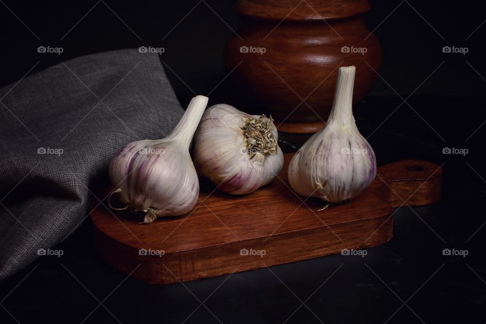 Still life with three heads of garlic on a wooden board in dark colors