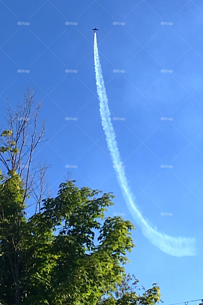 Going up!  Stunt plane show in rural Vermont.  Little plane against a brilliant blue sky with white smoke trailing behind. 