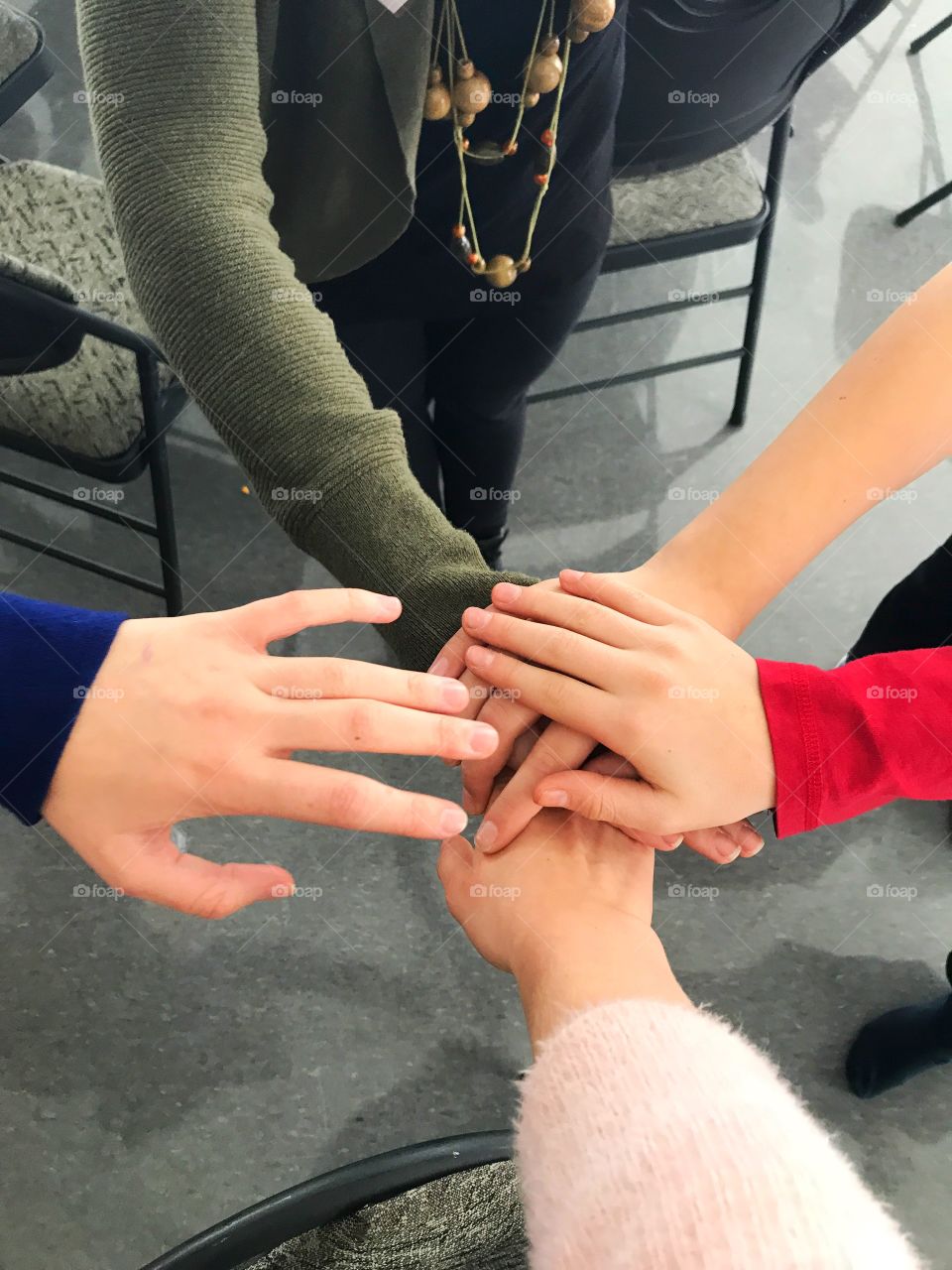Five hands of different skin tones and shirt colours and length and joining together in a center. There’s holding each other. There’s a look of solidarity.