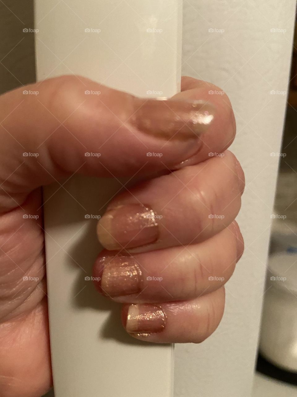 My hand with rose gold polished nails wrapped around a white freezer door handle 