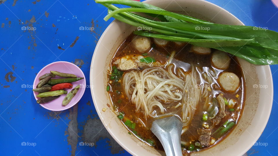 Thai noodle. hot noodle served with spicy grilled chilli and culantro vegetable on bright blue table background