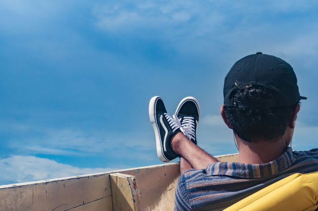 A rear view of a man sitting down on a front side of a boat, relaxing his feet, enjoying the fresh air