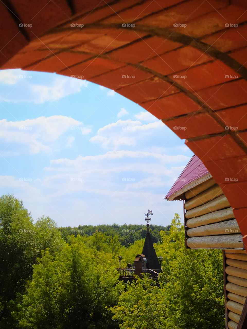 View from a brick window.  In the green forest, a wooden house with a spire