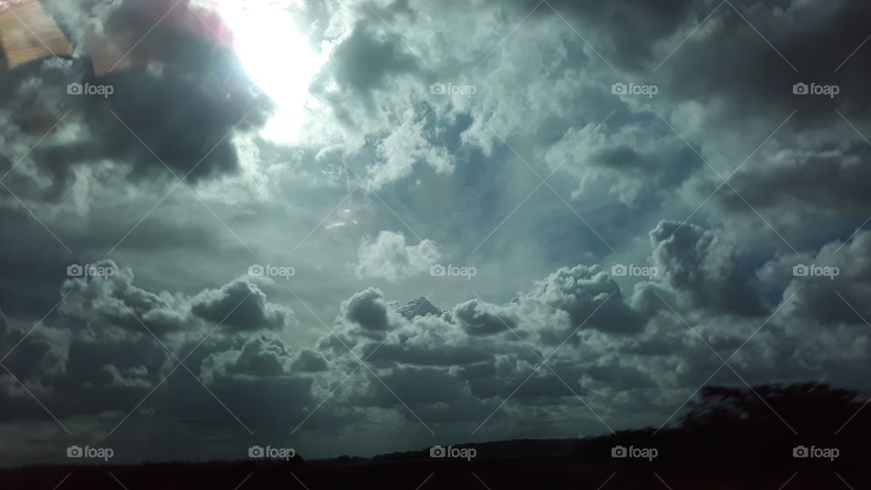 Sol entre nuvens, com um campo aberto na parte inferior da foto.