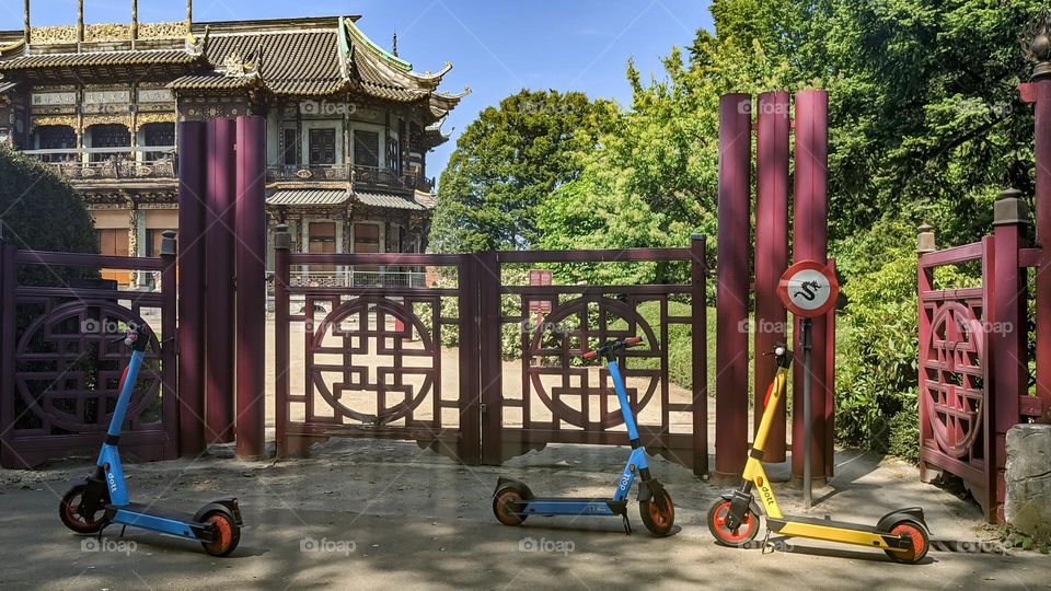 Beautiful view of three modern electric scooters parked near a house with Chinese architecture and iron gates on a summer sunny day in the city of Brussels, close-up side view.