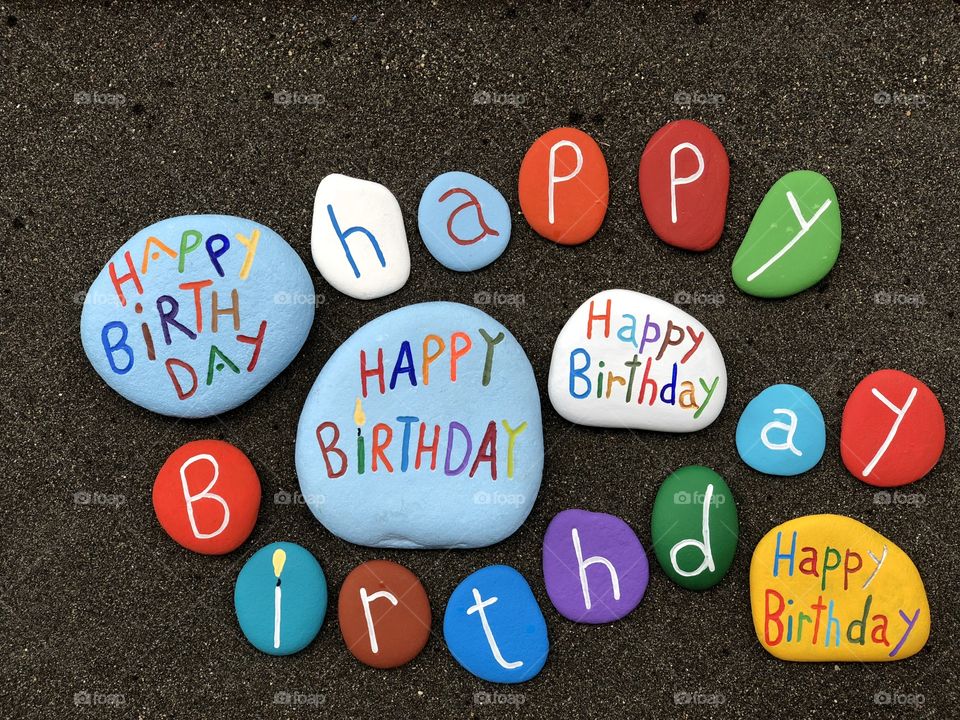 Happy Birthday funny multicolored stones over black volcanic sand 