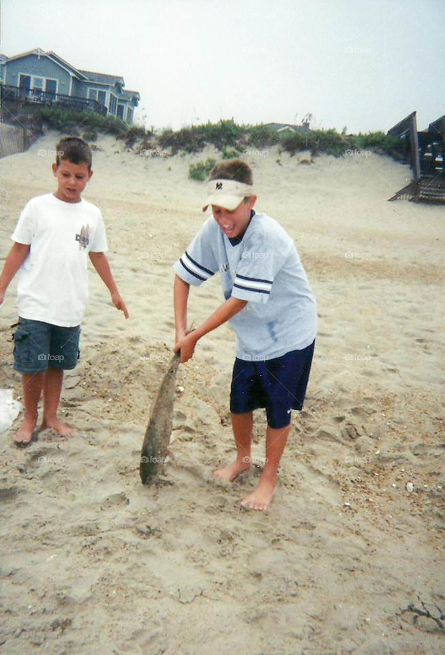 hauling in a big fish. Two boys delight in their catch on the beach in the Outer Banks of North Carolina