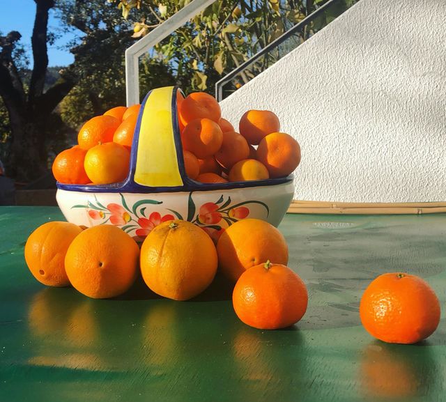 A ceramic fruit basket full of oranges outside on a green table