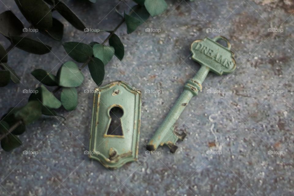 Light teal, metal vintage key with embossed word, “Dreams,” and keyhole on concrete surface 