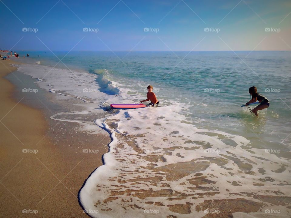 A young boy and girl surfing in the summer ocean waves.