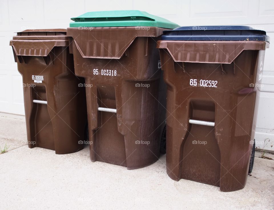 Ina row of waste bins against a white background the green lid on one of the bins distinguishes recycling from the other bins indicating keeping the earth green.