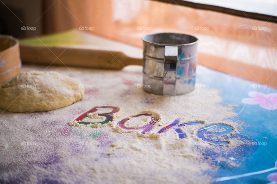 On the table lies a pastry for pies with sprinkled flour and a seeder for flour. Written to bake on the table.