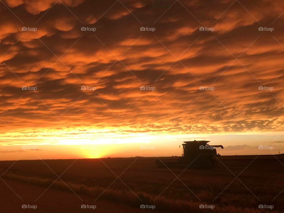Orange sunset sinking down behind John Deere tractor