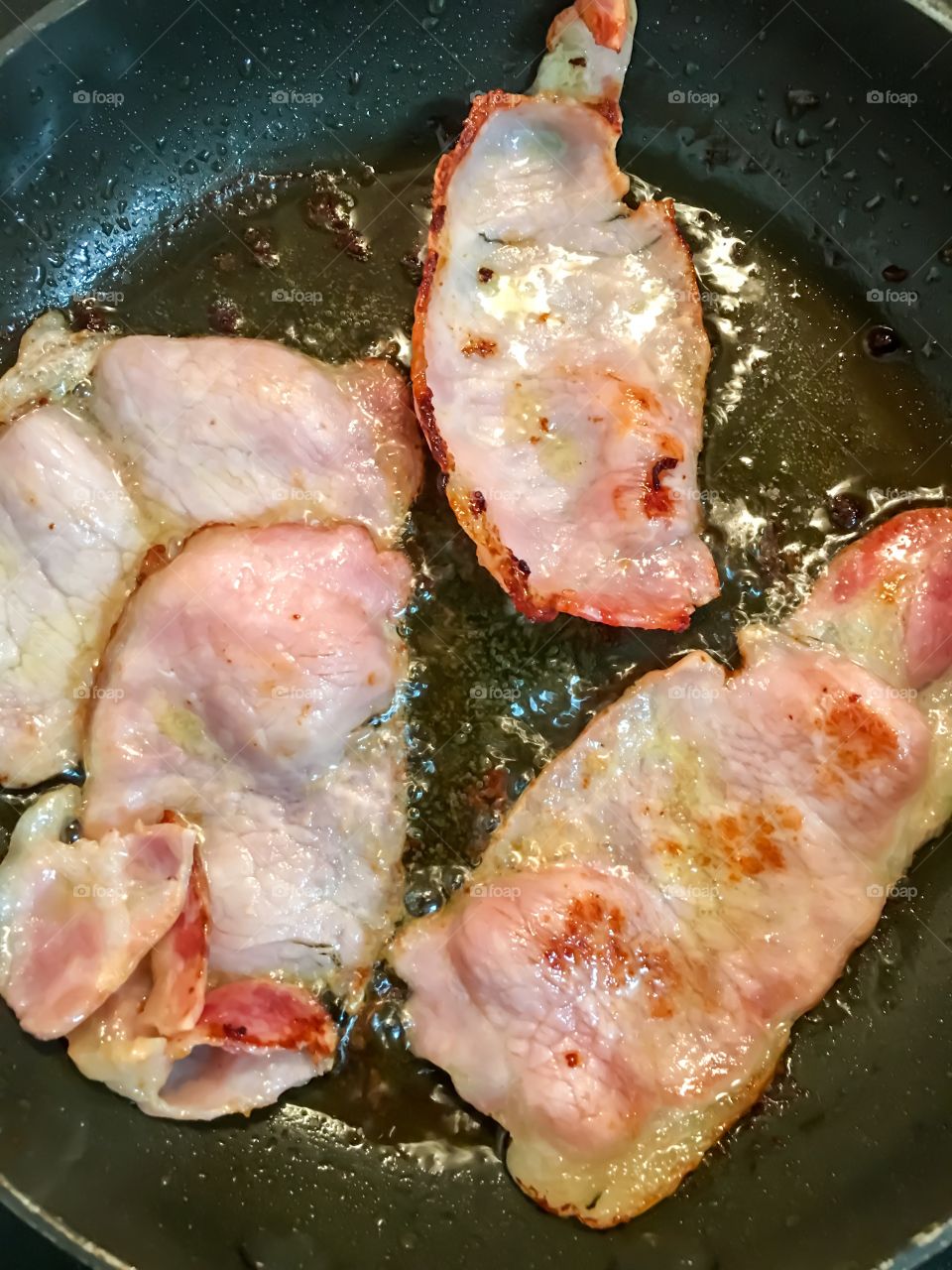 Shortcut pork bacon frying in fry pan closeup sizzle