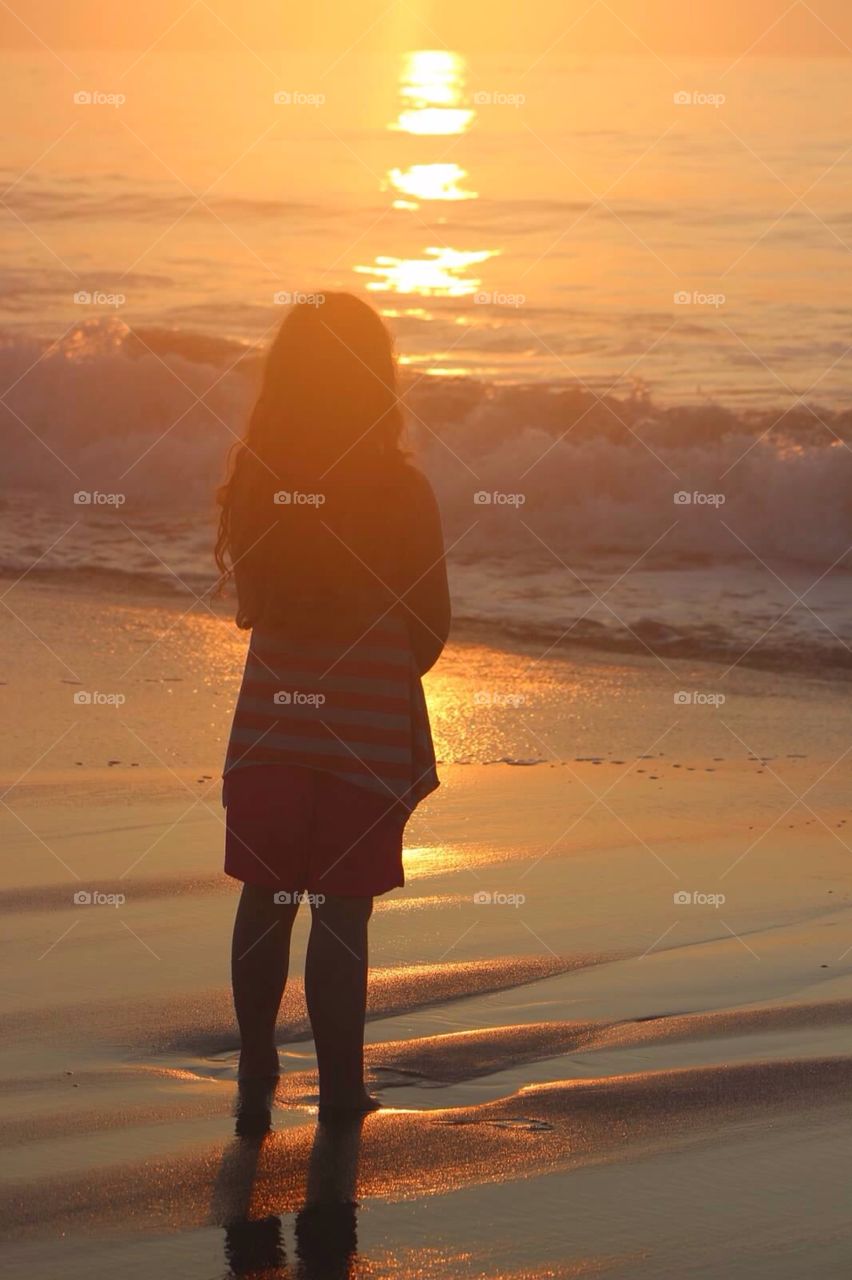 Watching the sun rise. . Young girl watching the sun rise over the horizon at the beach. 