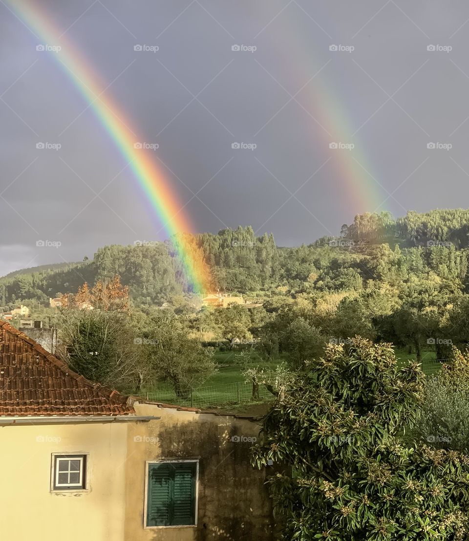 Double rainbow shines down on trees in a semi-rural landscape