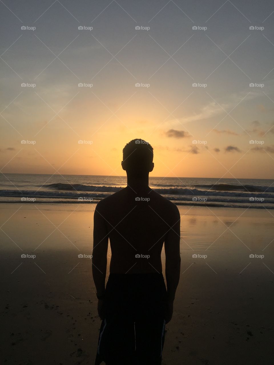 Silhouette of a young man standing in front of the rising sun at the beach