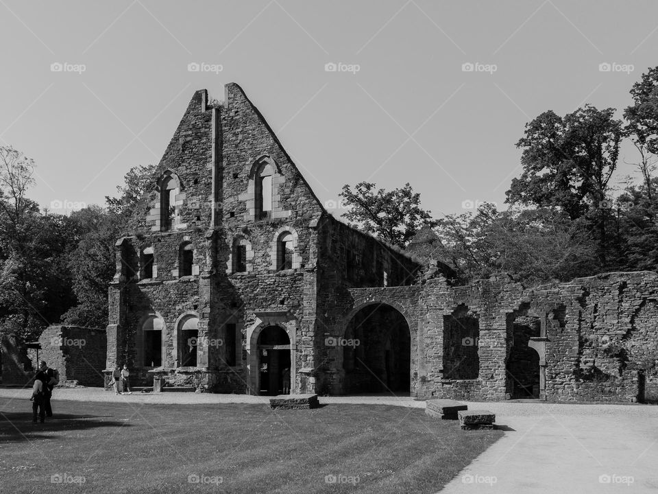 A beautiful view of the ruined walls and frame of the Villers-la-Ville monastery among trees and a lawn with a path in Belgium, close-up side view. The concept of the architecture of ancient monasteries and castles.