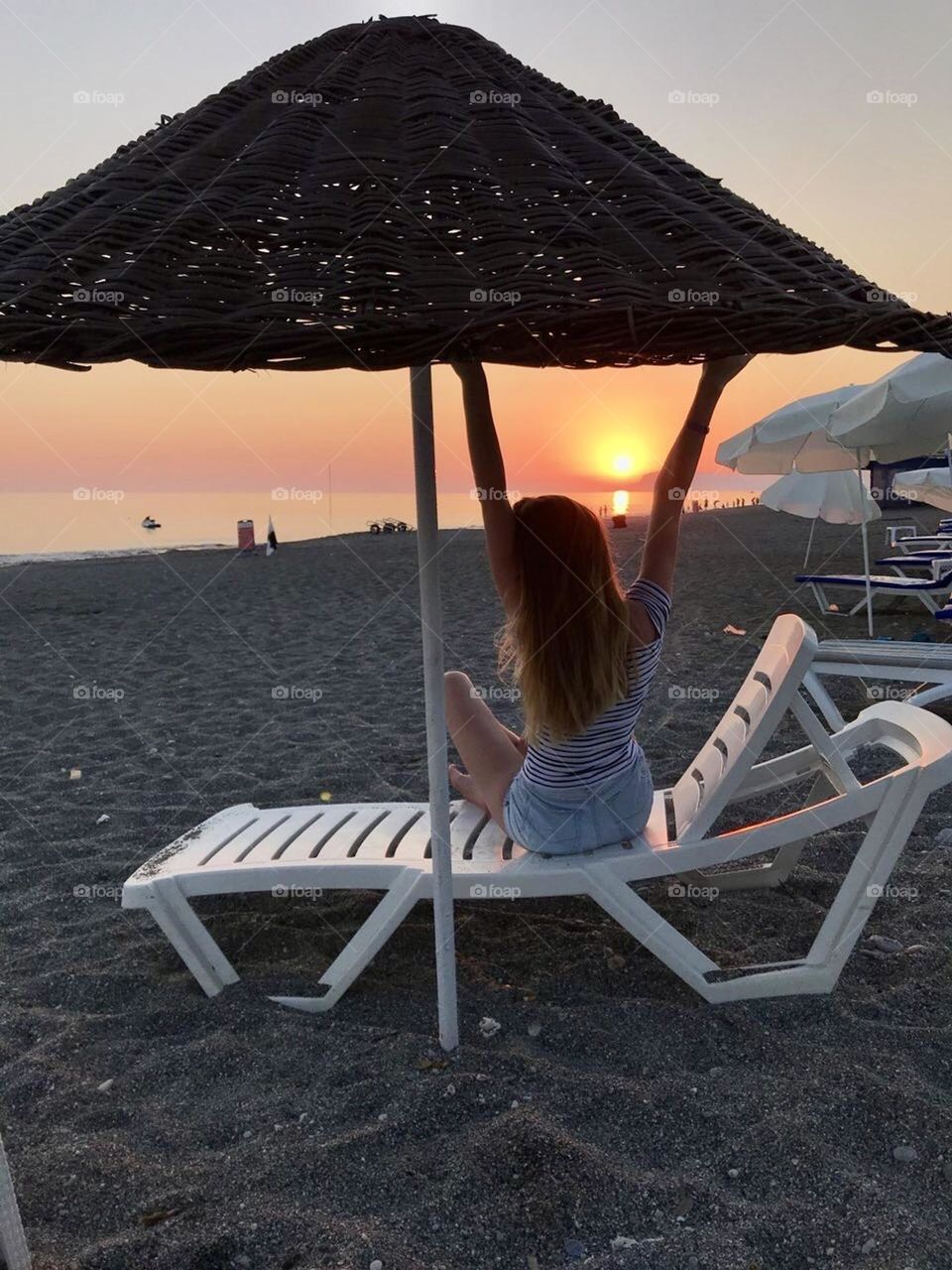 Её силуэт выделяется на фоне оранжевого неба, волосы колышутся на ветру. Девушка в восторге от красоты этого момента 