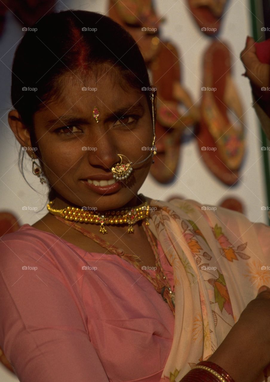 Golden facial jewellery on a bronzed Indian woman in Rajasthan, India. Of the many jewels an Indian woman displays around her body the nose ornament (nath) is perhaps one of the most eye-catching. The bindi, forehead jewel, is known as the third eye.