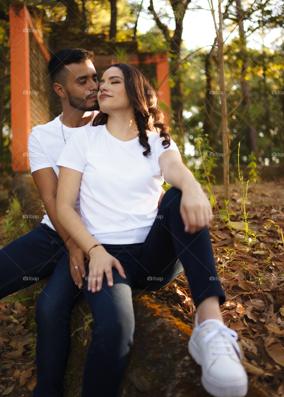 Couples of young people sitting in middle of the forest while looking smiling and happy, in a sunny day.