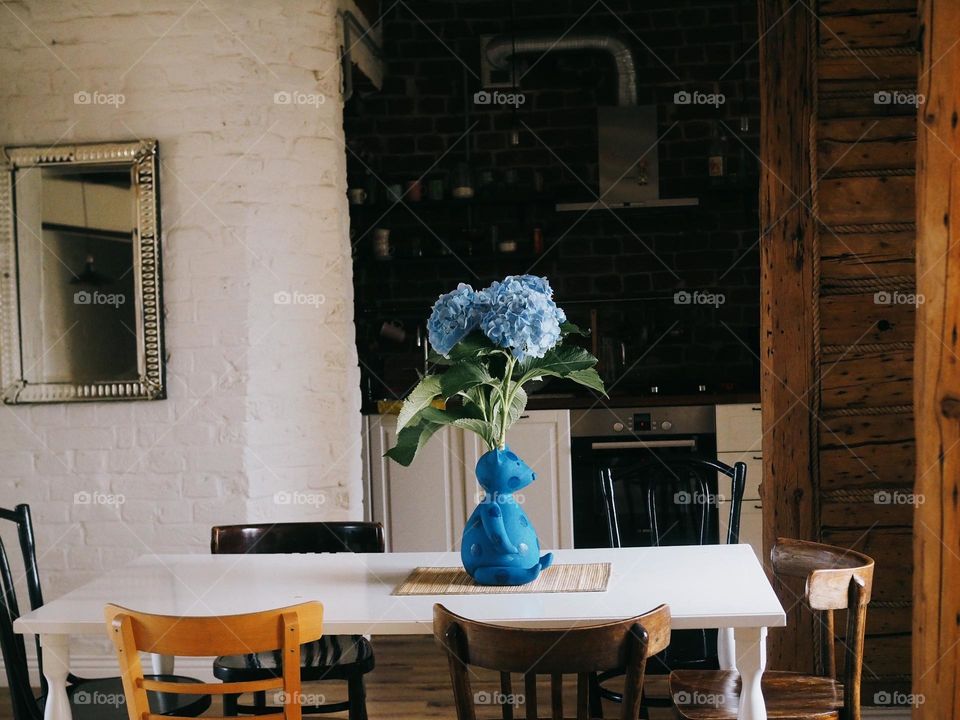 Bouquet of blue hydrangeas in general in the shape of a bear stands on a wooden table in a cozy kitchen