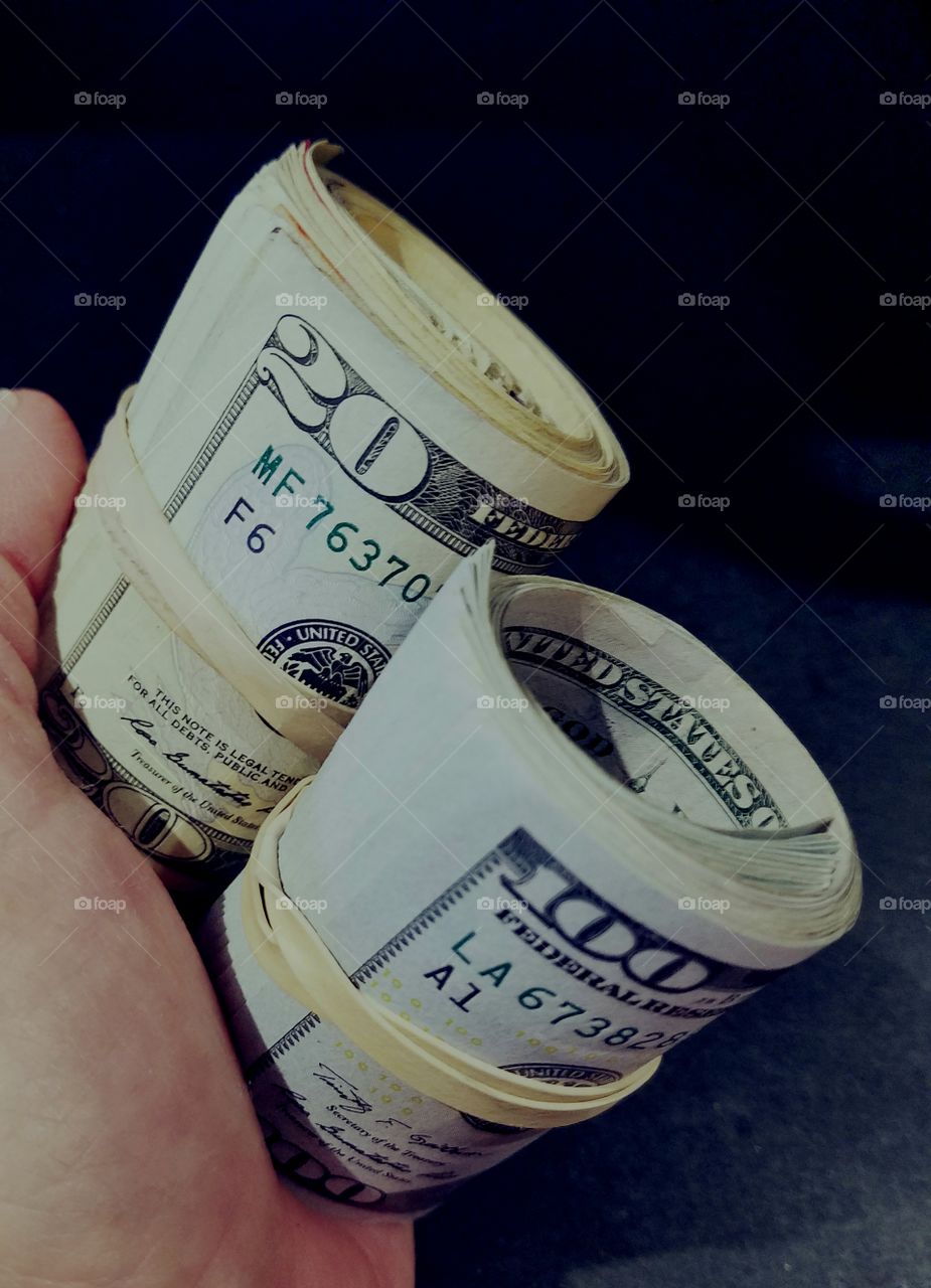 U.S. cash $20s & $100s money rolled up being held in hand.