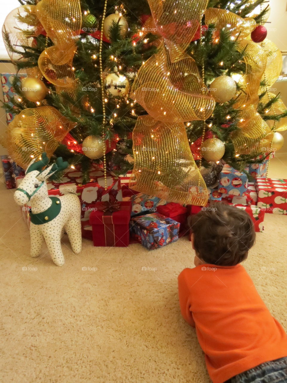 Little boy laying in front of Christmas tree daydreaming of opening his gifts.