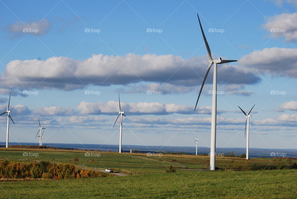 Windmills standing in a green farm hay field landscape with blue sky and clouds