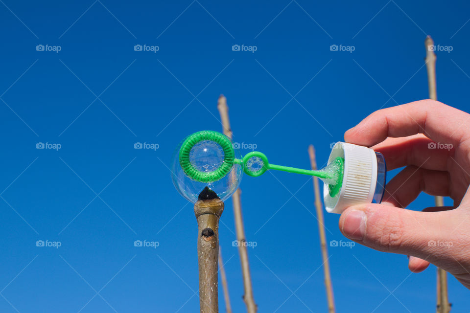 Man trying to put a single soap bubble on top of a plant stem