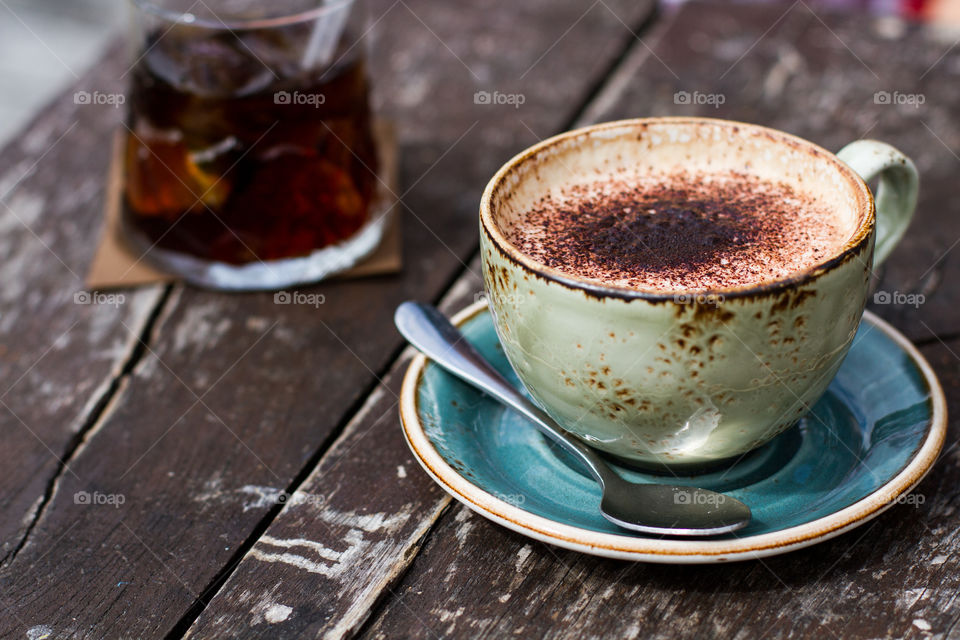 A cappuccino coffee in a distressed up and saucer on a wooden table top.