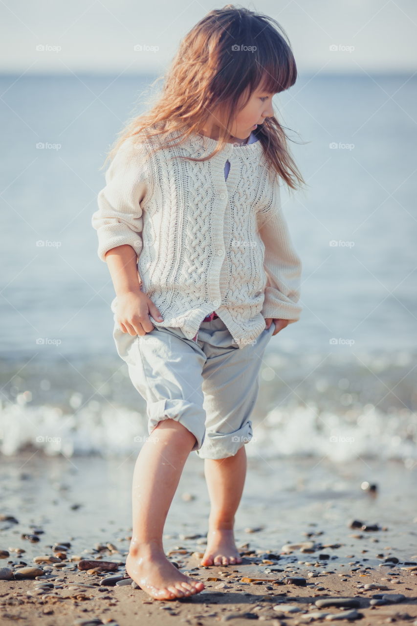 Little girl walking on the sea shore at sunny morning 