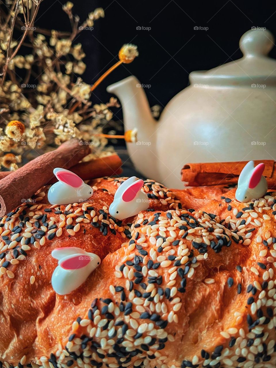 Miniature rabbits searching for food on top of sesame bread with a bug teapot at the back